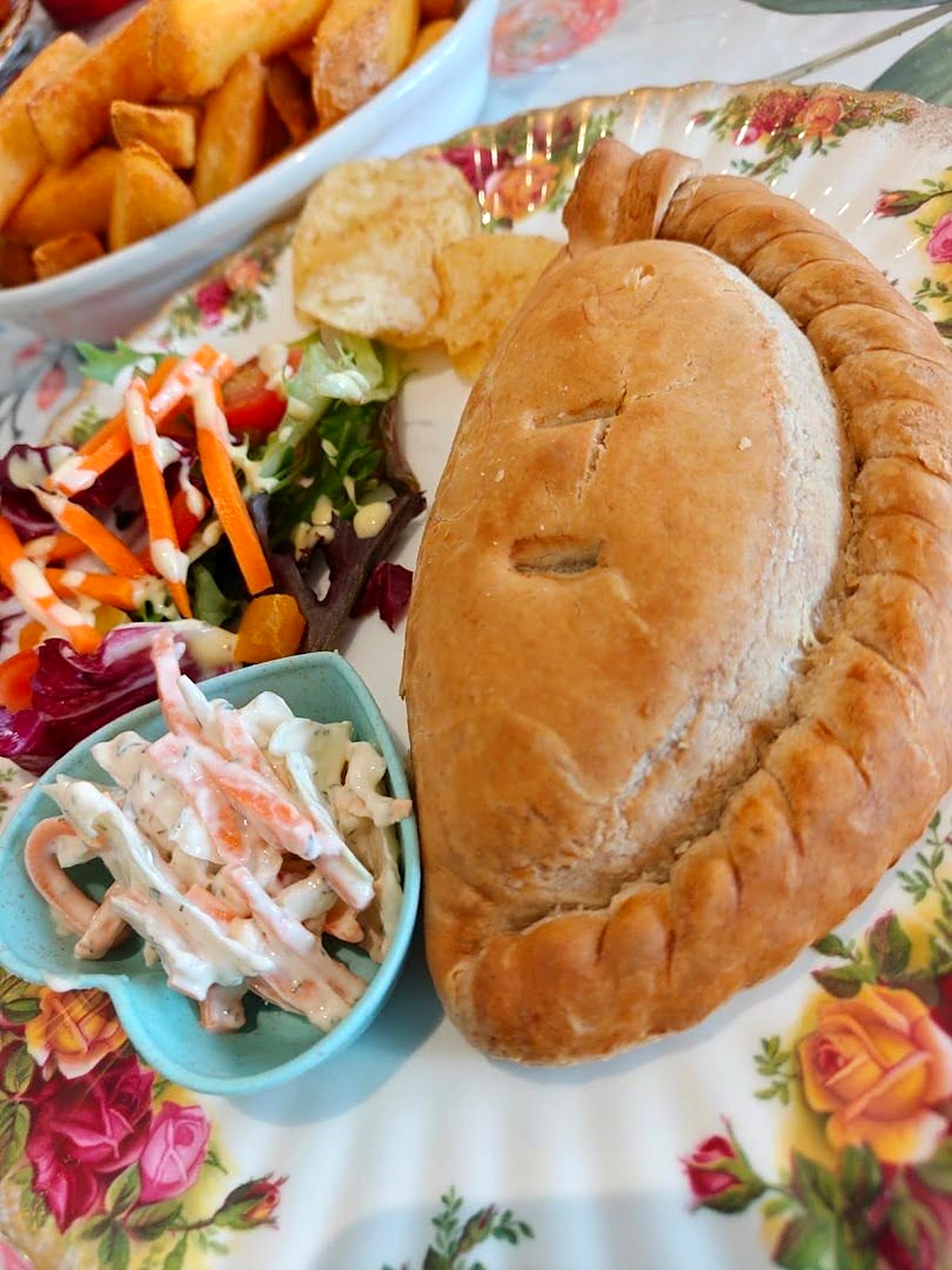 A golden pasty with salad and coleslaw on a plate printed with roses