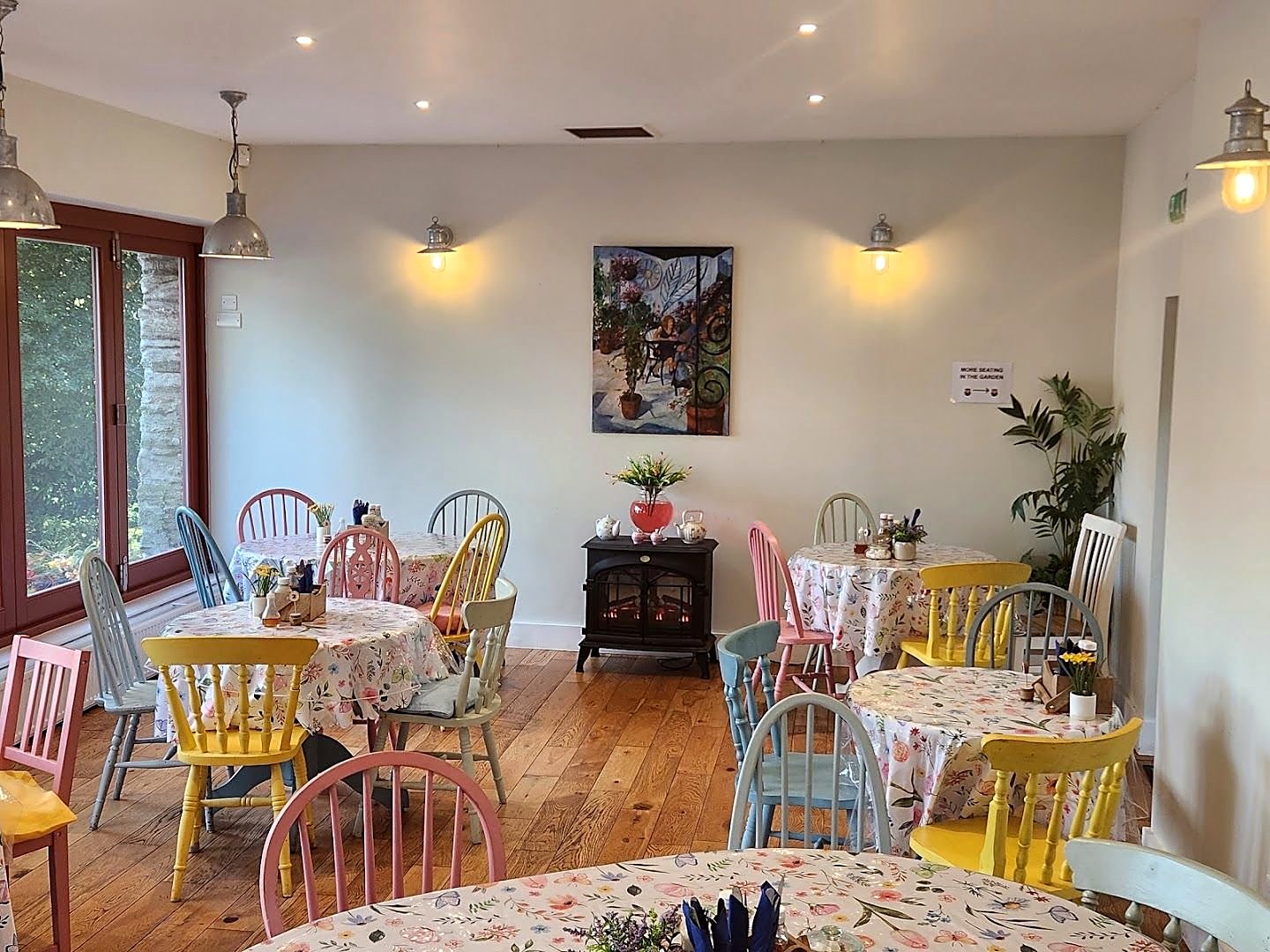 Inside the tearoom: flowered tablecloths, yellow, pink and blue painted chairs, wooden floor and a picture on the white wall